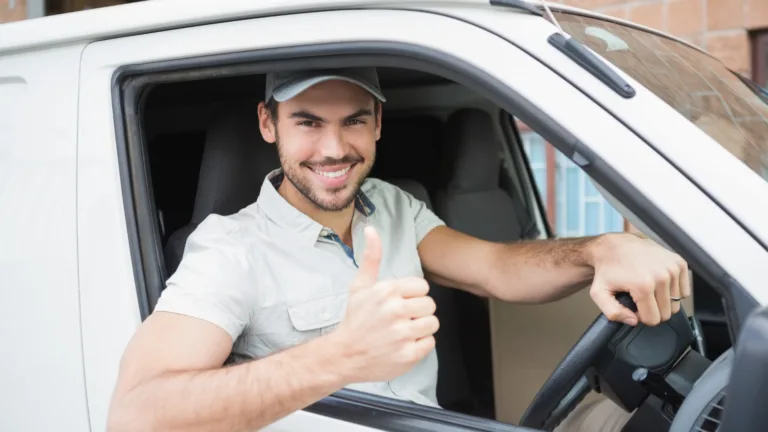 Conductor sonriente manejando una camioneta de carga blanca, el lleva gorra y camisa blancas